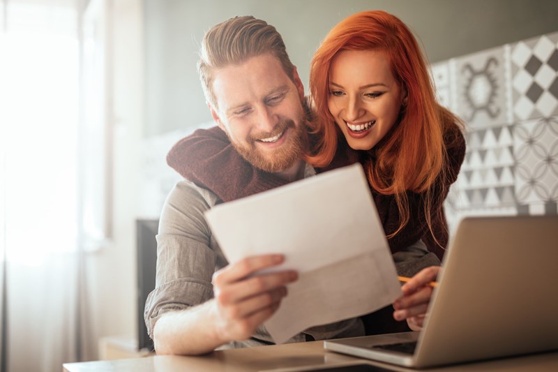 Photo of a positive young couple embracing and calculating the bills at home.